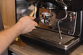 Crop anonymous male barista attaching portafilter with ground espresso coffee on coffee machine in kitchen