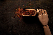 Top view of wooden scoop filled with natural aromatic ground sun dried tomato powder on artificial wooden hand on black background
