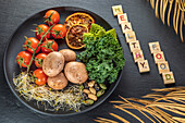 From above of decorative title near cooked potatoes with bunch of cherry tomatoes and sprouts on plate on gray background