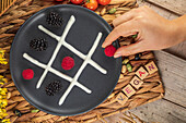 Top view of crop unrecognizable cook putting whole raspberry on plate with blackberries and whipped cream representing noughts and crosses game