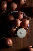 Closeup halved and whole unpeeled onions placed in bowl on shabby table on black background