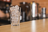 Transparent glass of ice cubes prepared for refreshing beverage placed on wooden countertop in bar