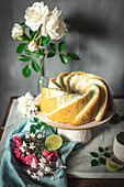 Tasty lime sponge cake served on white plate near flowers and lime slices