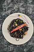 From above black spaghetti with squid ink garnished with prawns and sprouts and served on plate during lunch in restaurant