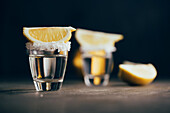 Tequila shots with salt and lemon placed on reflective surface against dark background