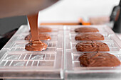 Cropped unrecognizable person in apron and gloves filling plastic mold with liquid chocolate during work in confectionery in daytime