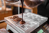 Cropped unrecognizable person in apron and gloves filling plastic mold on digital scale with liquid chocolate during work in confectionery in daytime