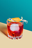 Glass of bitter alcoholic Negroni cocktail served with ice and orange peel on light surface