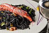 Black spaghetti with squid ink garnished with prawns and sprouts and served on plate during lunch in restaurant