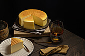 From above plates with tasty cotton cheesecake placed near glass of beverage on wooden table in dark room