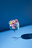 Transparent glass of fresh cocktail with mint leaves and flowers placed on surface against blue background