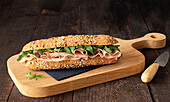 Mortadella ham sandwich with rocket leaves on wooden cutting board on rustic kitchen table