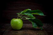 Whole ripe green apple with foliage and pure small aqua drips on black background