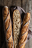 Top view of cut and whole sourdough baguettes with crunchy crust placed on wooden table