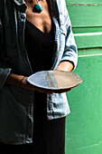 Crop unrecognizable artisan in apron demonstrating creative ceramic plate in workshop