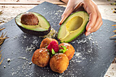 From above of crop anonymous cook with ripe avocado halves near appetizing deep fried croquettes with raspberry on top