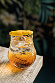 From above of tiki glass mug with booze placed on edge of wooden table in room with colorful curtain on blurred background
