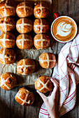 From above hand with appetizing freshly baked sourdough hot cross buns and mug of coffee on wooden table