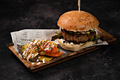 Yummy burger with vegetarian patty and grilled shiitakes between buns near sweet potato and carrot slices with alioli sauce on dark background