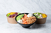 Bowls with delicious poke dish with assorted ingredients placed on marble table in kitchen