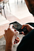 From above back view of unrecognizable male chef in uniform taking photo on cellphone of meal in bowl at restaurant