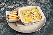 Pan with delicious provoleta cheese dish and bowl with ladyfinger biscuits placed on plate on gray marble table