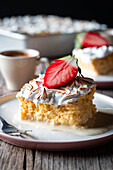 Sweet delicious piece of three milks cake with half fresh strawberry on white plate on wooden table