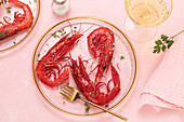 From above glass plate with tasty fried tiger shrimps placed near glass of wine on table pink background