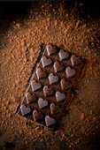 Ganze Schokoladentafel mit herzförmiger Dekoration von oben auf schwarzem Hintergrund mit gestreutem Kakaopulver serviert