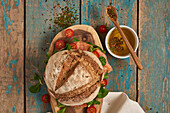 Draufsicht auf selbstgebackenes Sauerteigbrot mit Lachs, serviert auf einem hölzernen Schneidebrett mit Kirschtomaten auf einem schäbigen Tisch