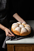 Blick von oben auf einen nicht erkennbaren Bäcker, der an der Theke steht und frische Brötchen auf ein Backblech in der Küche legt