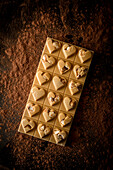 From above of whole chocolate bar with heart shaped decoration served on black background with scattered cocoa powder