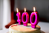 Burning candles with number 100 on sweet birthday cake prepared for celebrating and placed on table