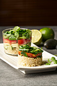 Blick von oben auf einen leckeren Salat aus Reis und Gemüse in runder Form und im Glas serviert auf einem weißen Teller neben grünen Limetten auf einem grauen Tisch