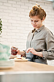Junge Frau mit Glas, die köstliches Beerengelee auf Pfannkuchen gibt, während sie am Tisch in der Küche kocht