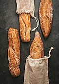 Top view composition of delicious crispy artisan sourdough bread loaves packed in burlap bags on black background