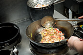 Hoher Winkel des anonymen Kochs, der Reis mit Gemüse im Wok brät, während er ein Gericht mit Garnelen in der Küche eines Restaurants zubereitet