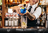 Crop unrecognizable female barkeeper squeezing fresh lime juice in glass while preparing Mojito cocktail at counter in bar