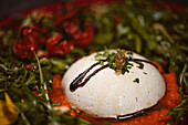 Yummy burrata cheese on cold tomato cream with arugula leaves and cherry tomatoes with truffles and peanuts