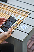 Ernte von oben, nicht erkennbarer Mann, der ein Smartphone benutzt und den QR-Code der Speisekarte eines Restaurants scannt