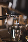 Frisch gebrühter Espresso fließt aus dem Einfüllstutzen einer professionellen Kaffeemaschine in einen rostfreien Milchkrug