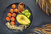 Top view of fresh half of avocado near bunch of cherry tomatoes and sprouts with Romanesco broccoli and nuts on plate