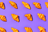 Draufsicht auf viele leckere Croissants, die ein nahtloses Muster auf hellviolettem Hintergrund bilden