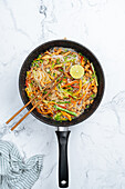 From above chopsticks on tasty stir fry rice noodles with vegetables served in frying pan