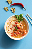 Tom yum soup in bowl with chopsticks on blue background