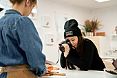 Crop female with fresh squash on cutting board against ethnic girlfriend taking photo on digital photo camera in house kitchen