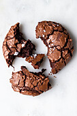 Top view of homemade baked broken sweet chocolate brownie cookie with cracks and crumbs placed on white background in light kitchen