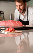 Raw fish fillet placed on cutting board on table in Asian sushi restaurant on background of blurred male cook