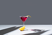 Composition of glass filled with red fruit cocktail near orange slides and zest placed on concrete table against grey background