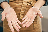 Crop unrecognizable female in apron showing palms of hands with flour after cooking in house